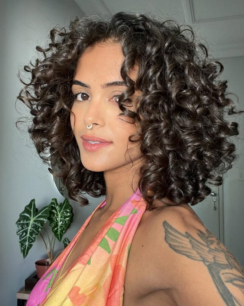 Mulher de pele preta-clara, com blusa estampada e cabelo crespo preso em camadas