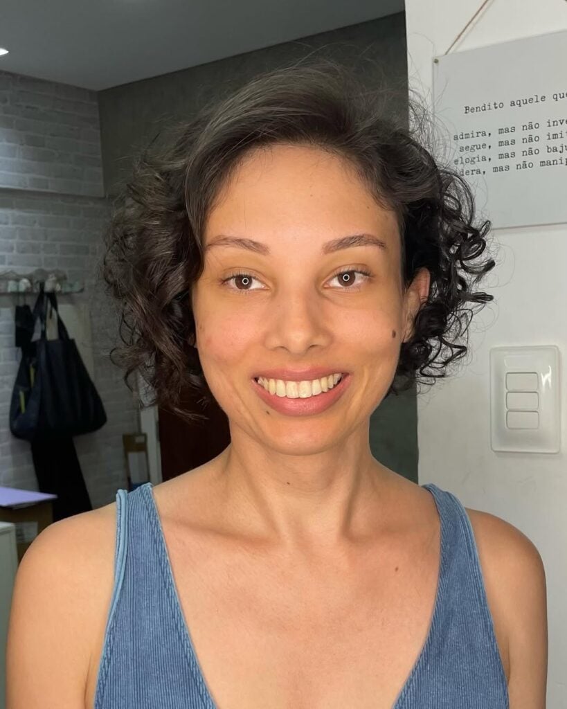 Mulher de pele clara, com blusa azul e cabelo curto cacheado com corte short bob