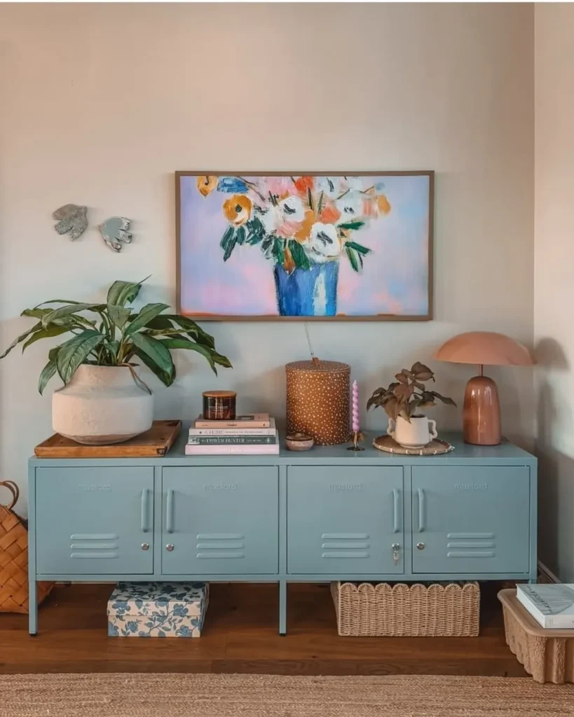 Armário azul com objetos decorativos e quadro com flores na parede