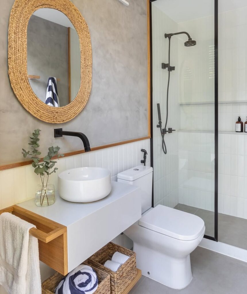 Banheiro branco com detalhes em metal preto fosco e meia parede atrás do espelho em cimento queimado