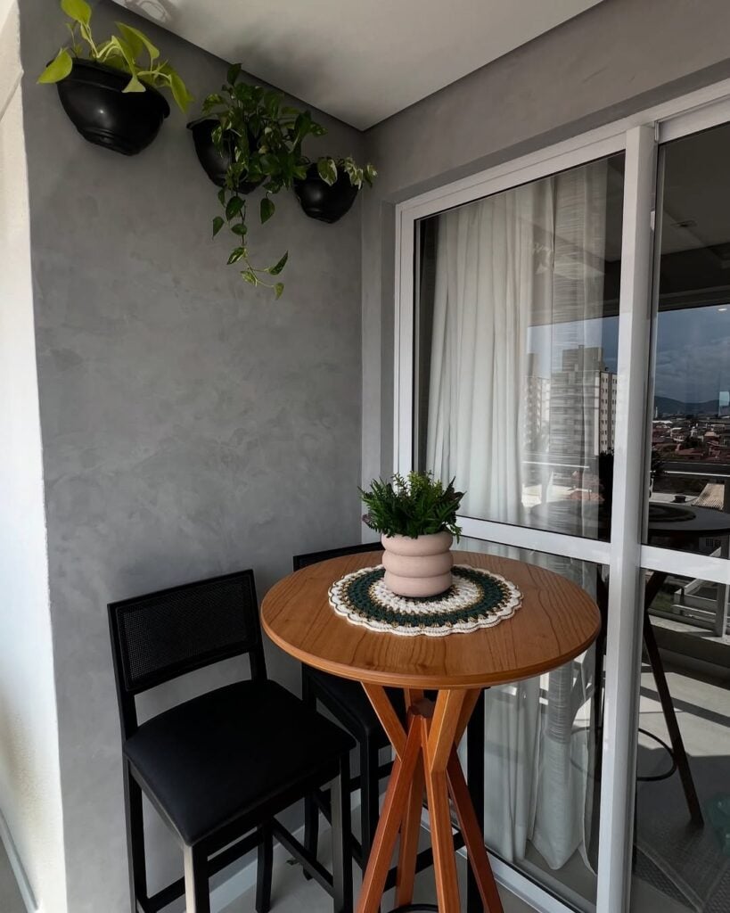 Varanda com mesa no estilo bistrô de madeira, cadeiras pretas e parede com cimento queimado cinza