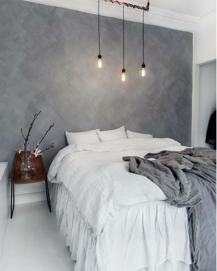 Quarto de casal com parede de cimento queimado cinza e pendentes finos