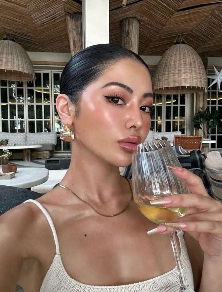 Mulher de pele clara, com cabelo escuro preso, acessórios em dourado e maquiagem clean