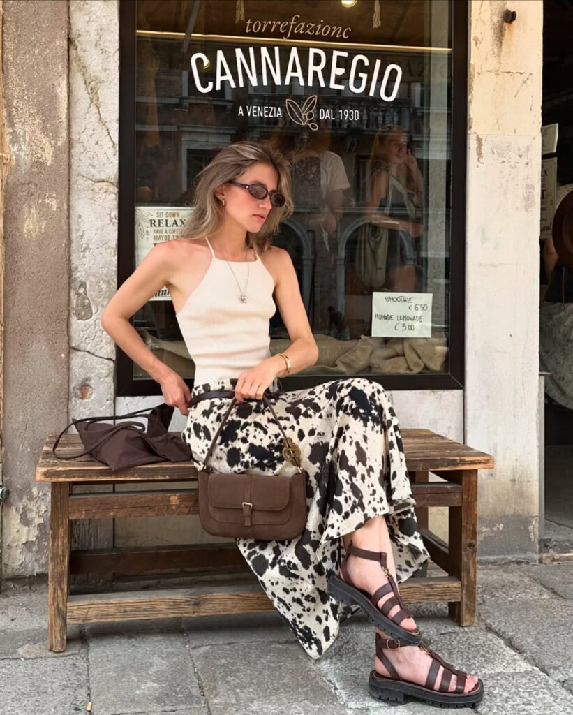 Mulher de pele clara, com blusa clara, saia cow print e sandália fisherman