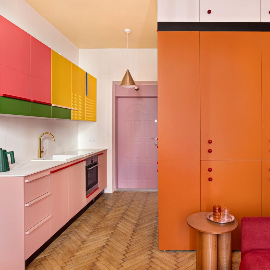 Cozinha com armários coloridos em laranja, rosa, amarelo e verde, e balcão da pia rosa