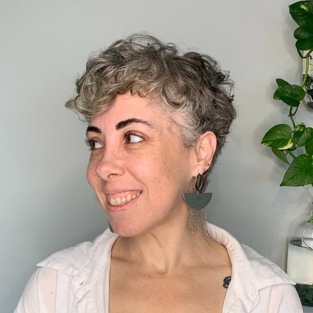 Mulher de pele clara, com blusa azul, brinco verde e cabelo loiro big chop