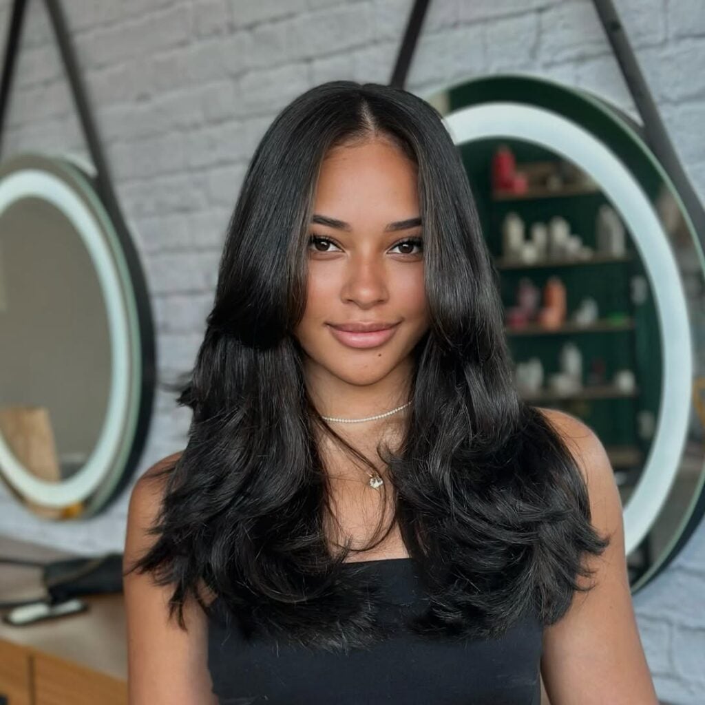 Mulher de pele preta-clara, com blusa escura e cabelo preto shaggy longo