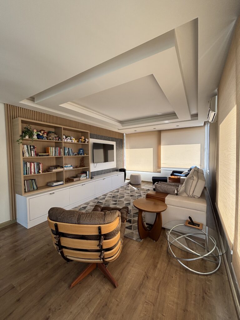 Sala de estar com estante amadeirada para livros, armário e painel de tv brancos
