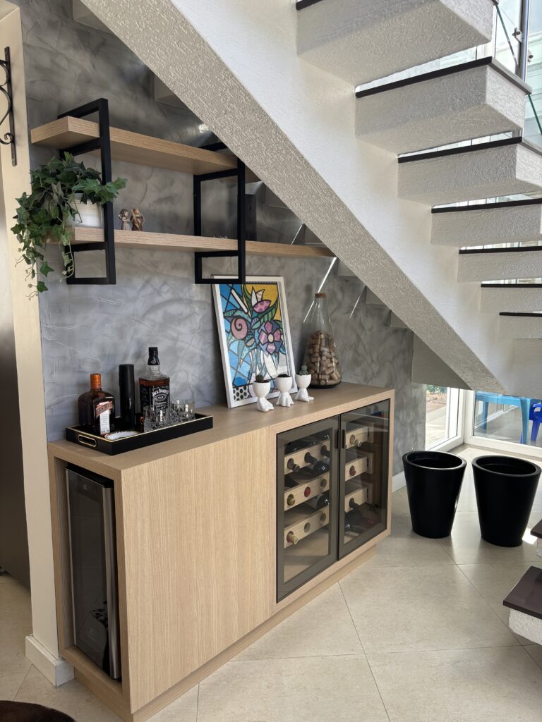 Adega de madeira abaixo da escada com objetos decorativos e prateleiras