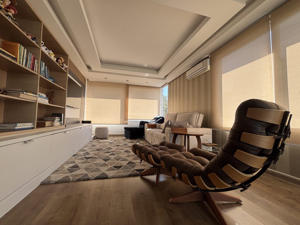 Sala de estar com teto de gesso, estante de livros e tapete com figuras geométricas