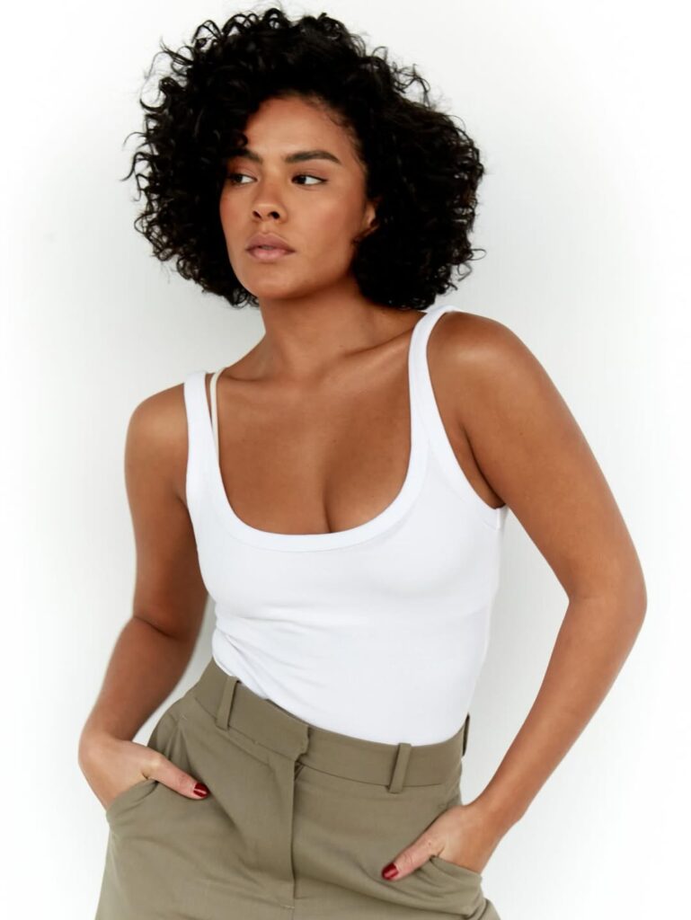 Bella Campos, com cabelo escuro, regata branca e calça de alfaiataria