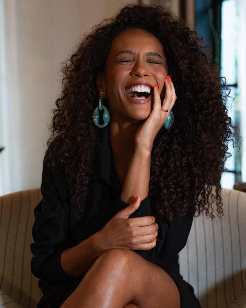 Taís Araujo com cabelo cacheado, brincos azul e unhas alaranjadas