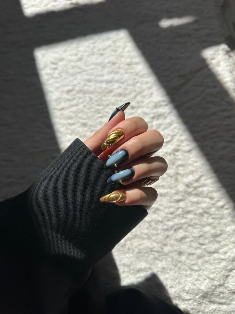 Mão de pele clara, com unha amendoada com dourado e design aura em azul