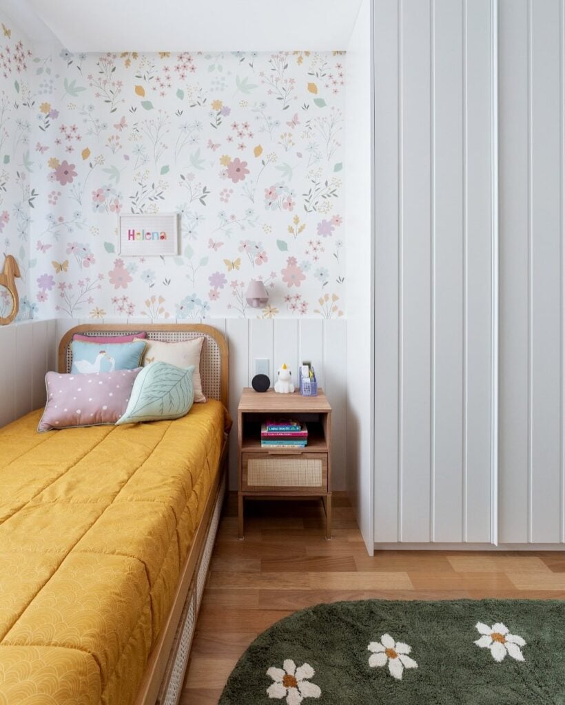 Quarto de solteiro com papel de parede com florzinhas e tapete verde com flores brancas