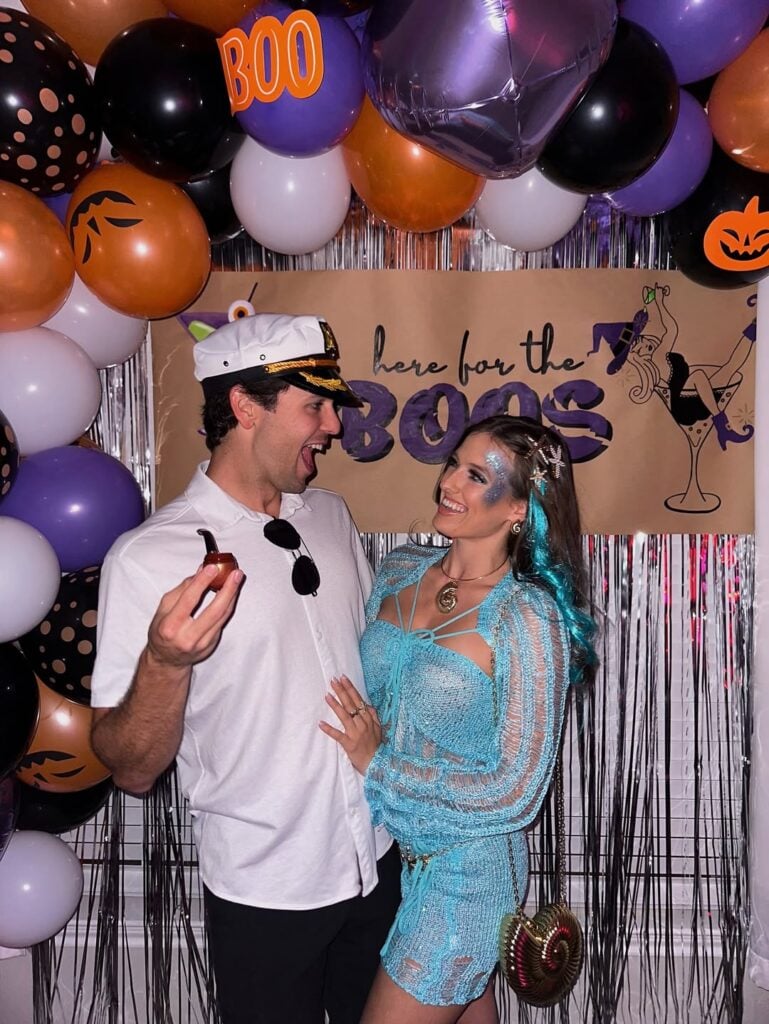 Casal jovem. Eles estão em uma festa com decoração de Halloween e usam roupa de marinheiro e sereia.