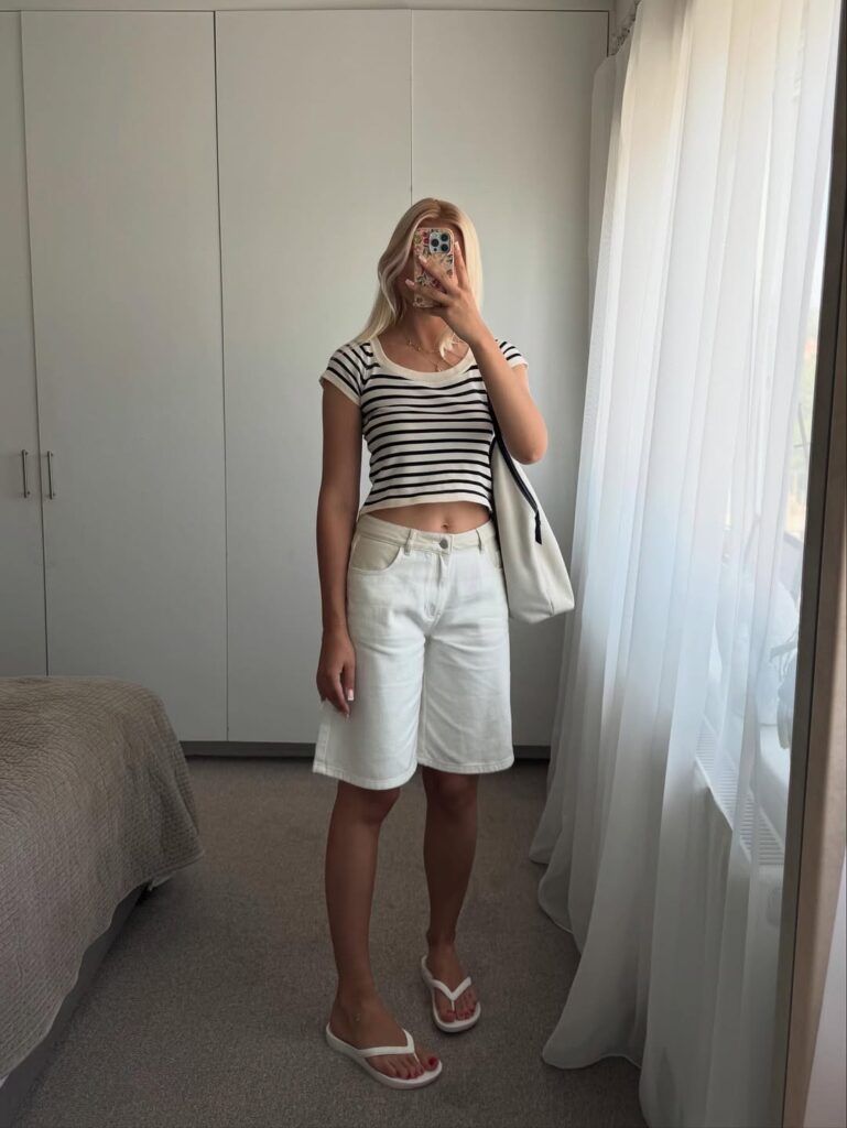 Mulher de pele clara, com cropped listrado, jorts branco e chinelo de dedo branco