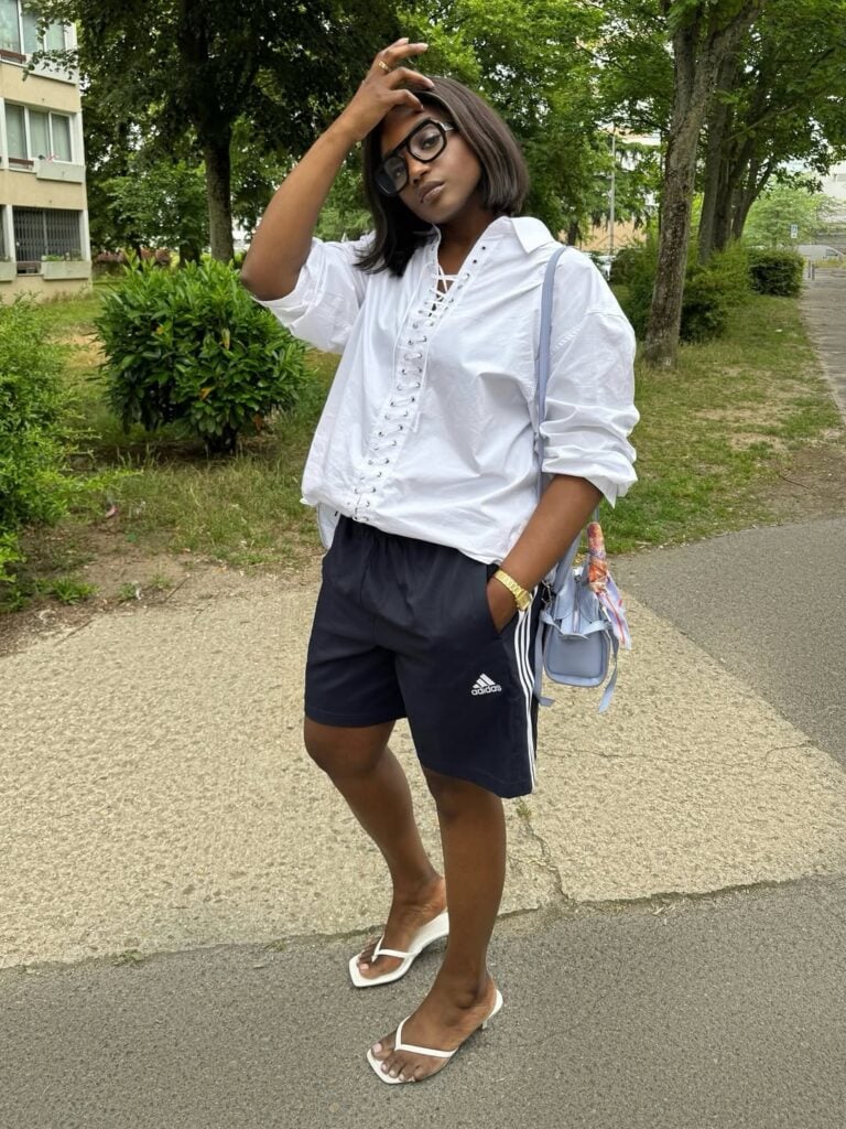 Mulher de pele preta, com cabelo curto, blusa branca, bermuda esportiva e chinelo kitten heels branco
