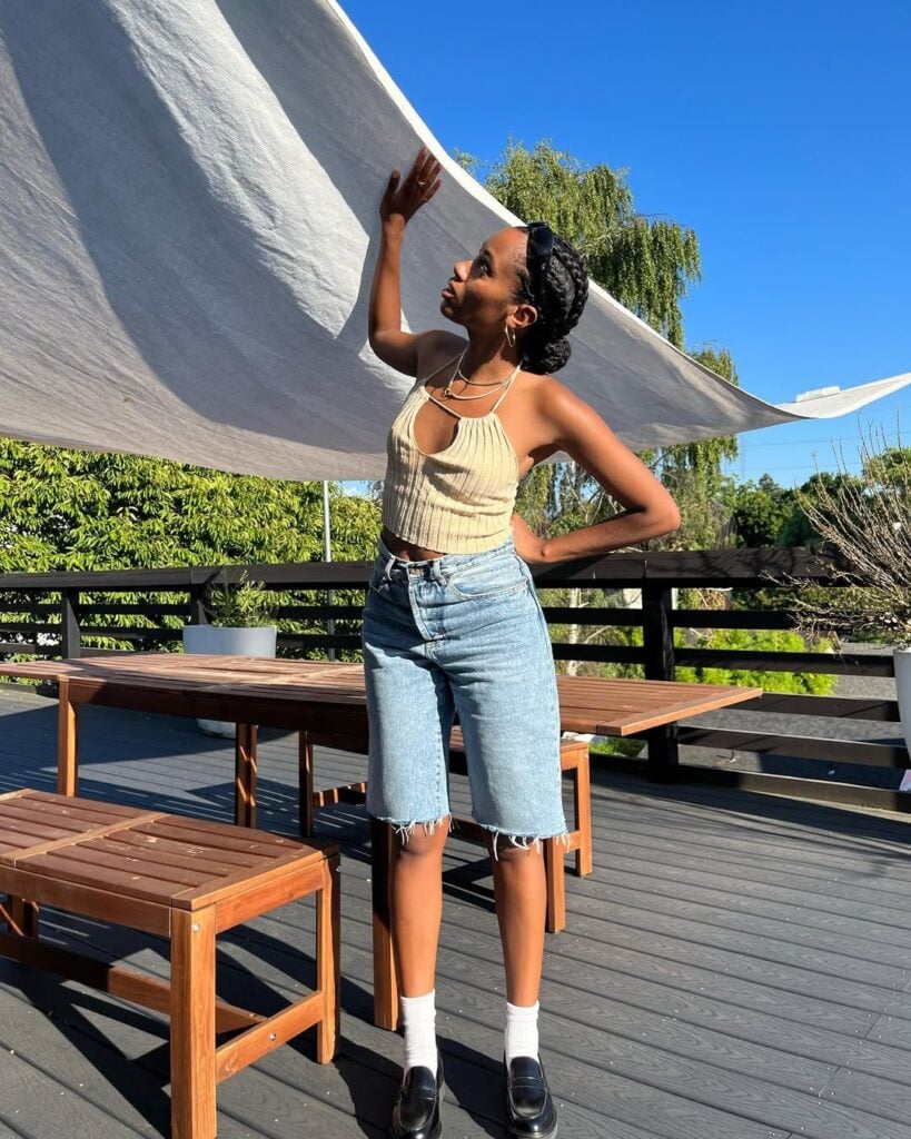 Mulher jovem usando bermuda jeans, top, mocassim e meia