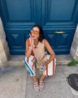 Mulher jovem sentada com regata, calça listrada colorida e sapatilha