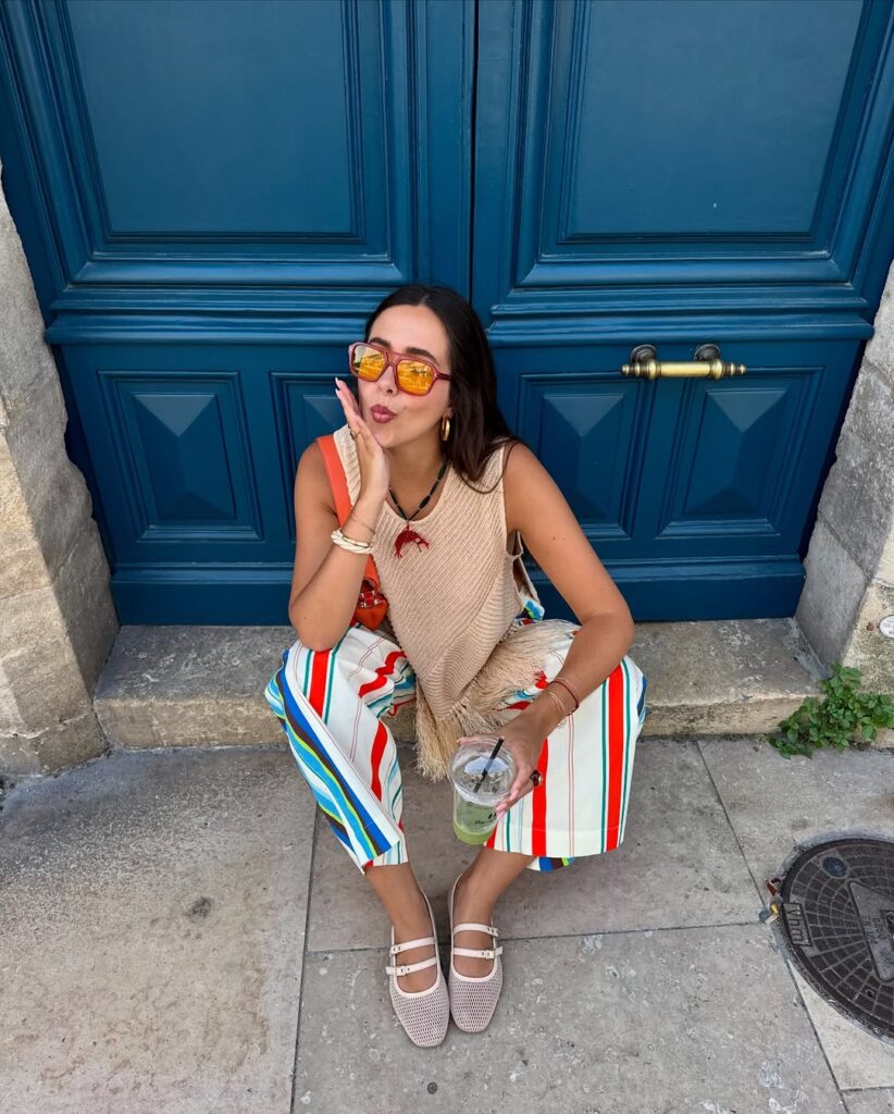 Mulher jovem sentada com regata, calça listrada colorida e sapatilha