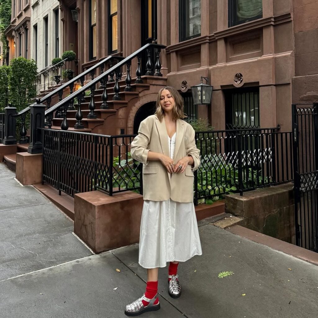 Mulher jovem com look de escritório composto por vestido, blazer e sandália com meias