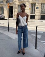 Mulher jovem e magra com look de escritório com blusa de cetim, calça jeans e salto alto
