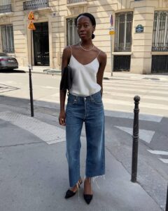 Mulher jovem e magra com look de escritório com blusa de cetim, calça jeans e salto alto