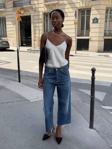 Mulher jovem e magra com look de escritório com blusa de cetim, calça jeans e salto alto