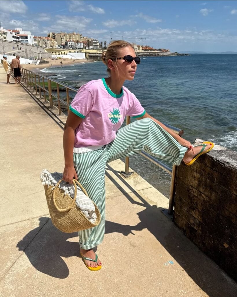 Mulher jovem com calça listrada, camiseta rosa e chinelo de dedo