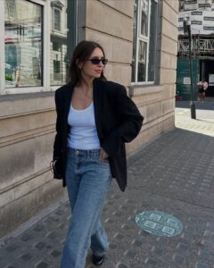 Mulher jovem e magra andando na rua. Ela veste blazer, regata e calça jeans.