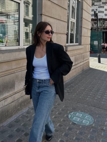 Mulher jovem e magra andando na rua. Ela veste blazer, regata e calça jeans.