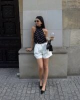 Mulher jovem com look em preto e branco composto de blusa de poá e bermuda branca
