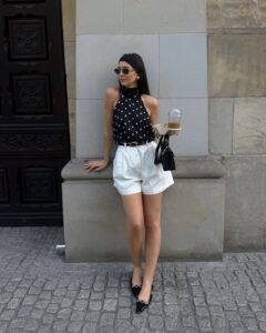 Mulher jovem com look em preto e branco composto de blusa de poá e bermuda branca