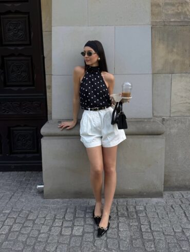 Mulher jovem com look em preto e branco composto de blusa de poá e bermuda branca