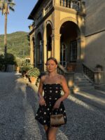 Mulher de pele clar,a com cabelo preso, vestido de poá e bolsa marrom