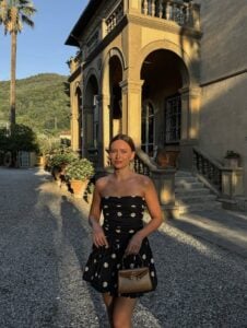 Mulher de pele clar,a com cabelo preso, vestido de poá e bolsa marrom