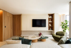 Sala de estar com painéis de madeira clara e natural, poltrona verde orgânica e mesas de centro com vaso de flores