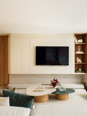 Sala de estar com painéis de madeira clara e natural, poltrona verde orgânica e mesas de centro com vaso de flores