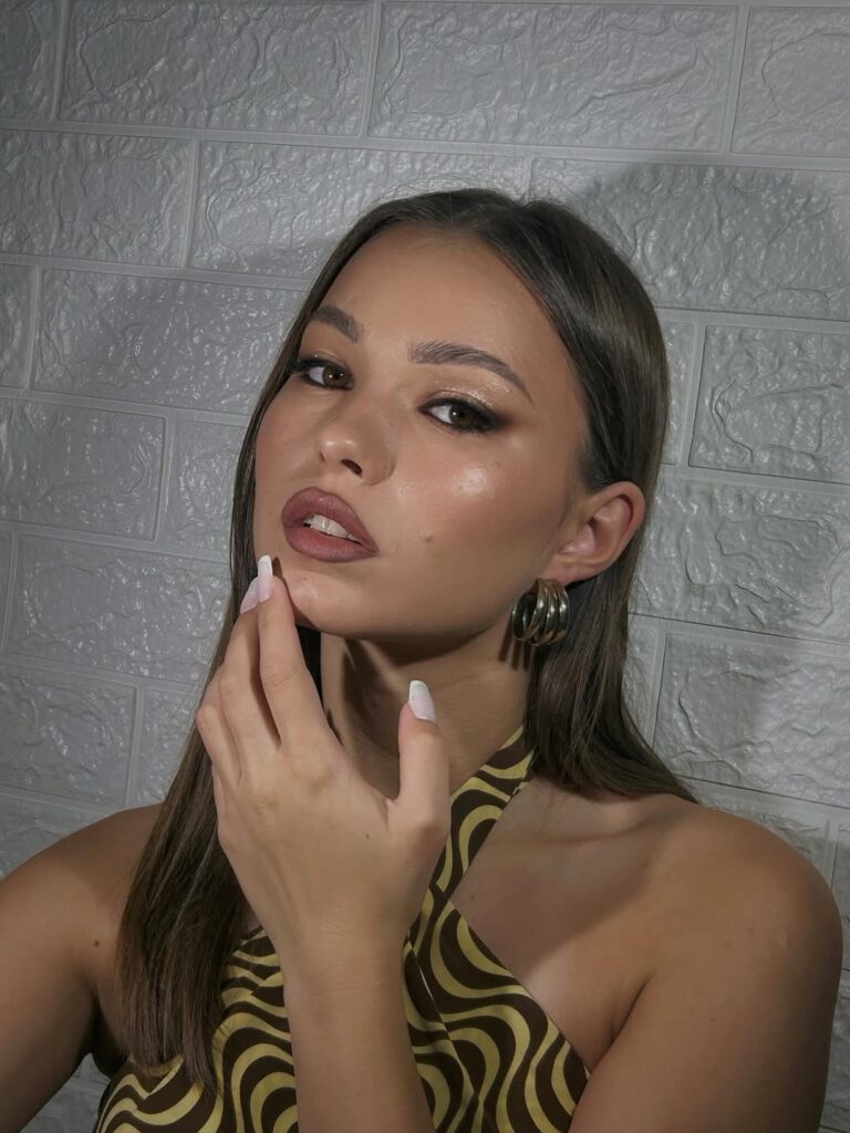 Mulher de pele clara, com cabelo loiro acinzentado e maquiagem marrom 
