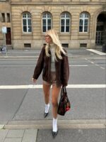 Mulher jovem com casaco, blusa, bermuda, sandália e meia branca