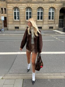 Mulher jovem com casaco, blusa, bermuda, sandália e meia branca