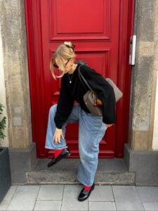 Mulher jovem com look de inverno composto por jeans, suéter e mocassim