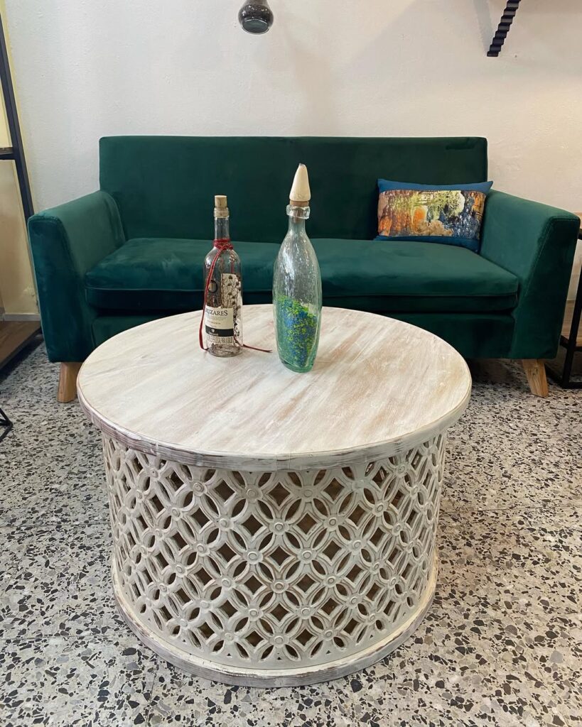 Sala com sofá verde em veludo e mesa de centro talhada em branco