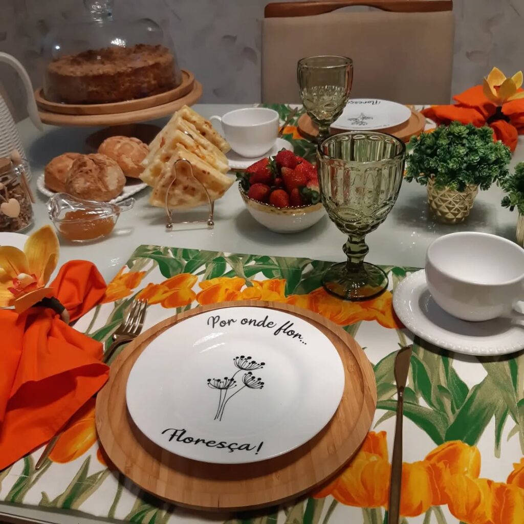 Mesa posta com jogo americano com tulipas laranja, bandeja de bambu e prato branco com flores