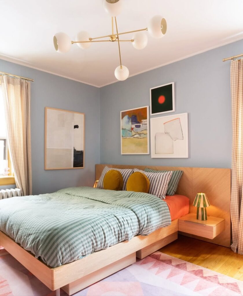Quarto de casal com parede em azul suave, roupa de cama listrada e almofadas amarelas