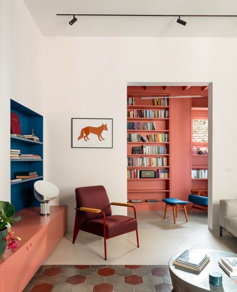Sala de estar com poltrona bordô, estante azul embutida na parede e ao fundo estante rosa
