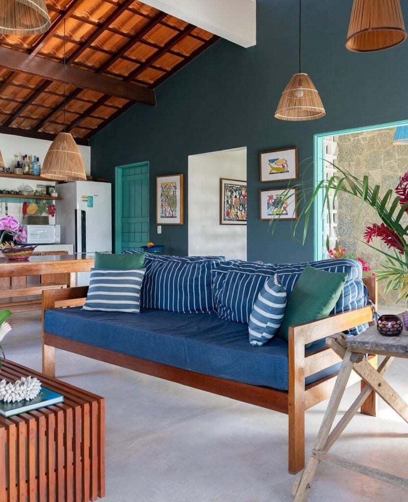 Casa com parede em tom de verde, sofá de madeira com almofadas azuis pendentes de fibras naturais