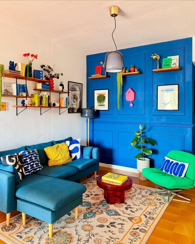 Sala de estar com uma parede e teto brancos, e a outra azul, sofá azul com pés palito e poltrona verde