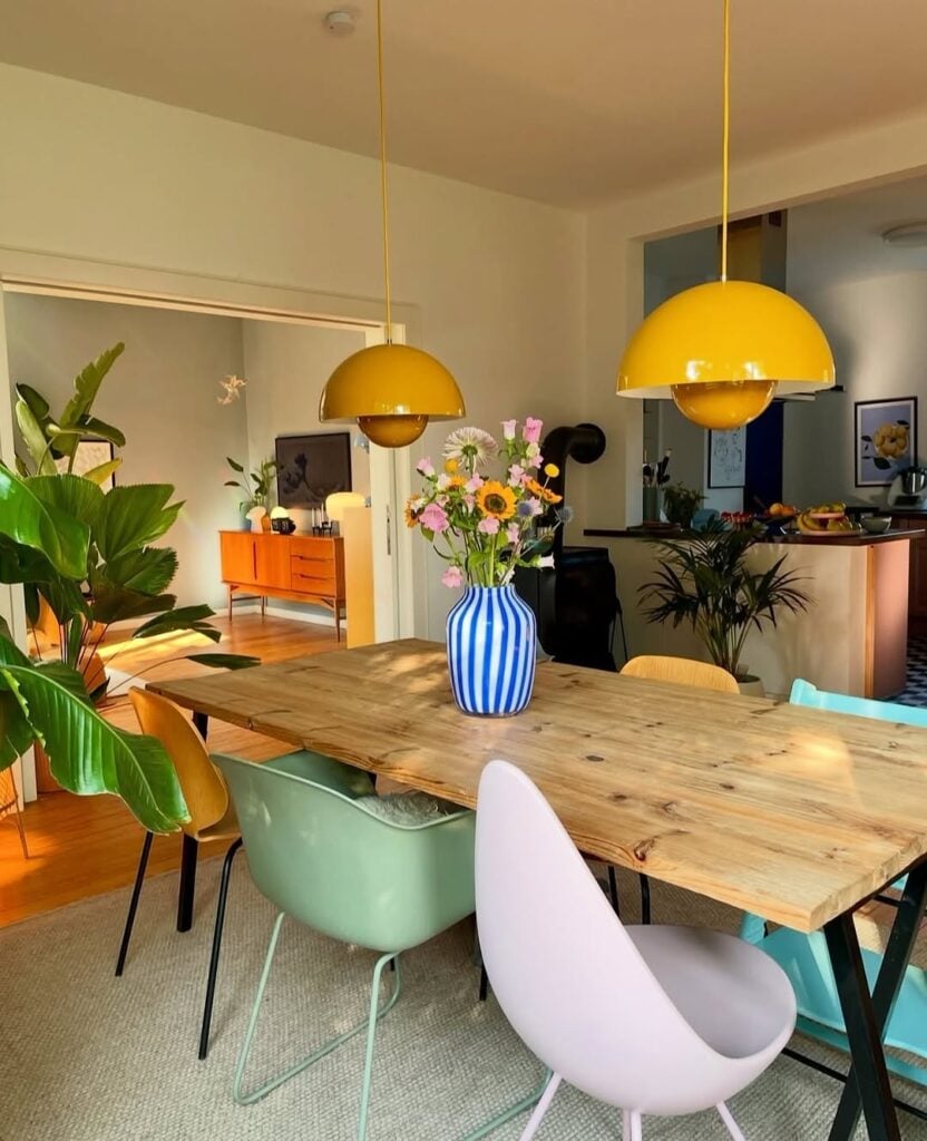 Sala de jantar com mesa de madeira, cadeiras de modelos e cores diferentes e pendentes amarelos