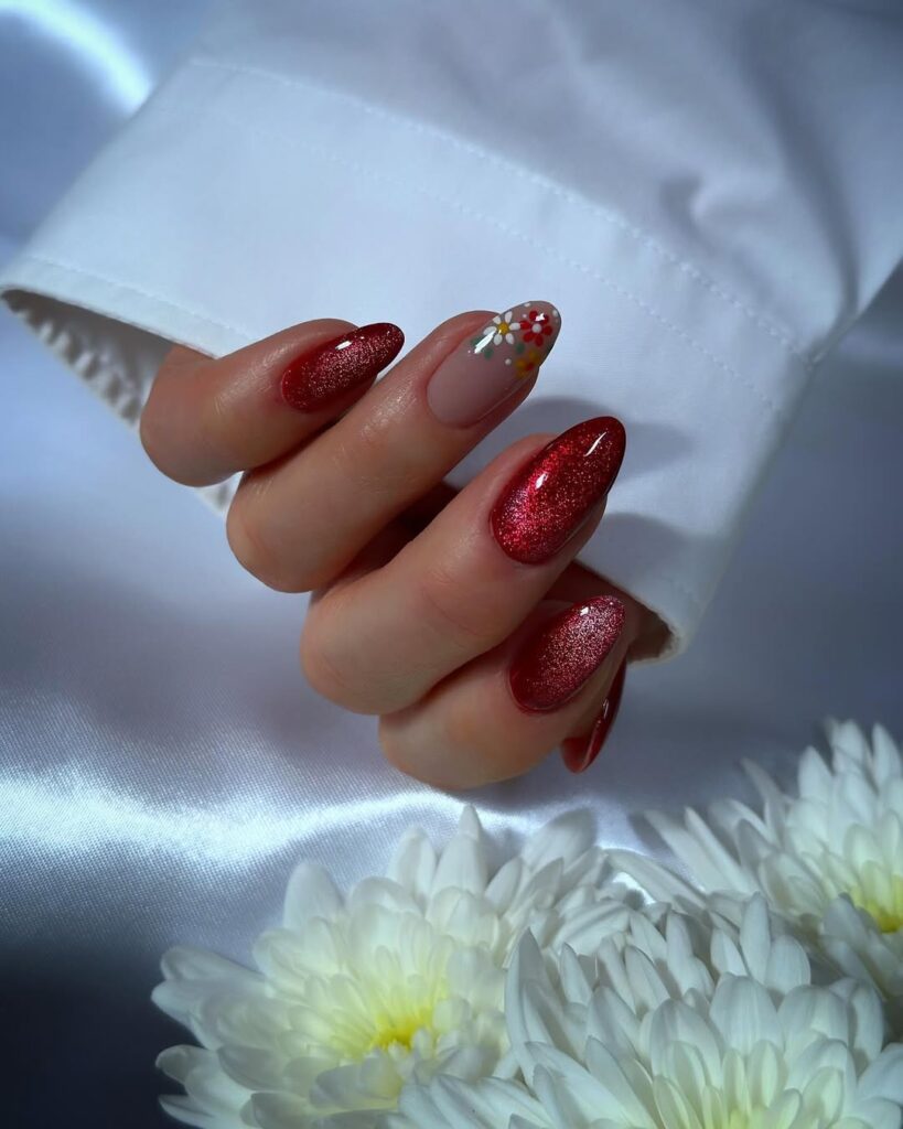 Mão de pele clara, com unha amendoada vermelha brilhosa e com decoração floral